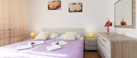 A neatly arranged bedroom with a bed, bedside tables, a dresser, and two wall-mounted paintings.