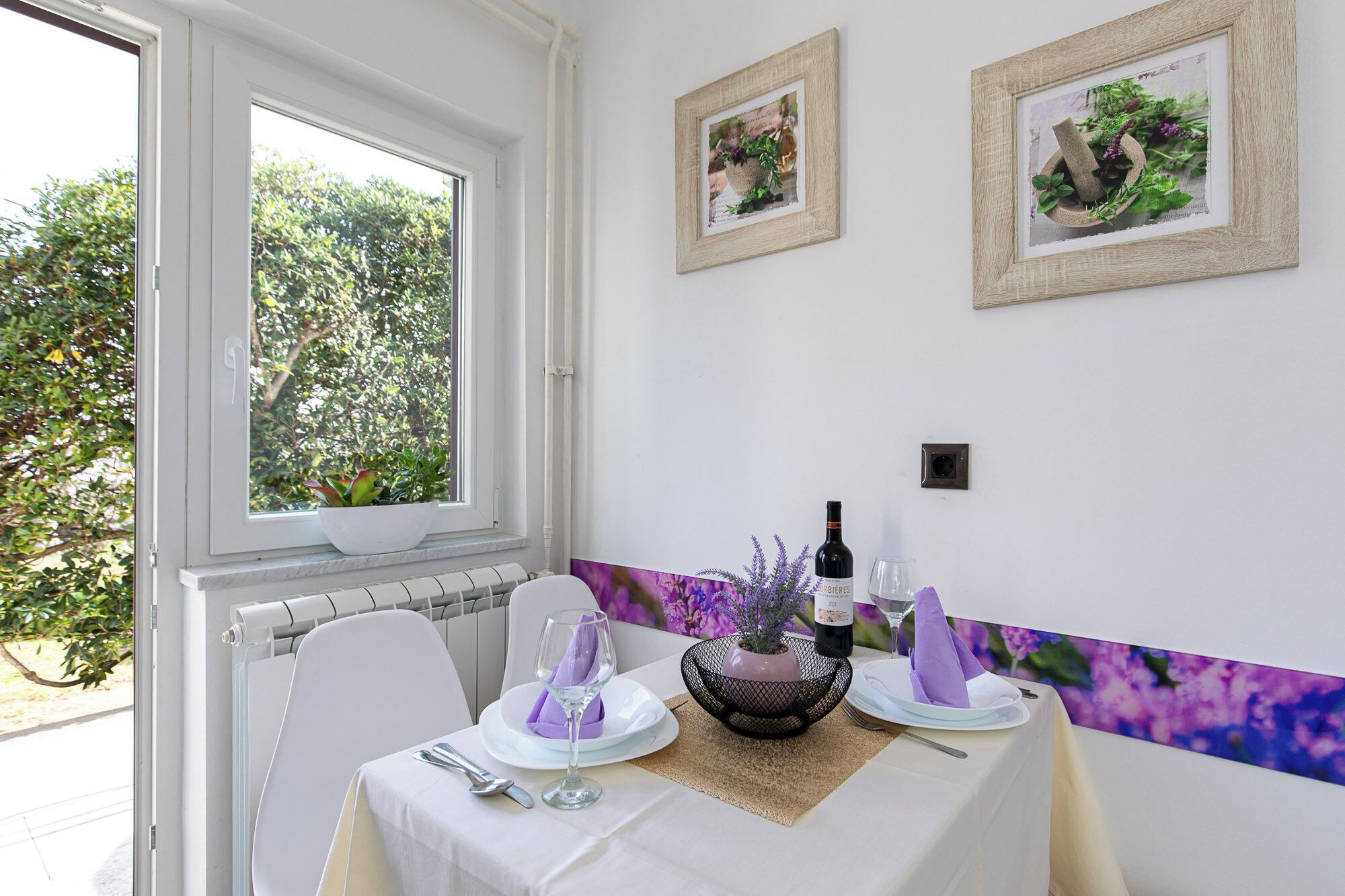 Un comedor con una mesa dispuesta para dos personas, una botella de vino y dos cuadros en la pared.