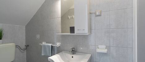 Un baño con un lavamanos blanco, un espejo encima y un inodoro.