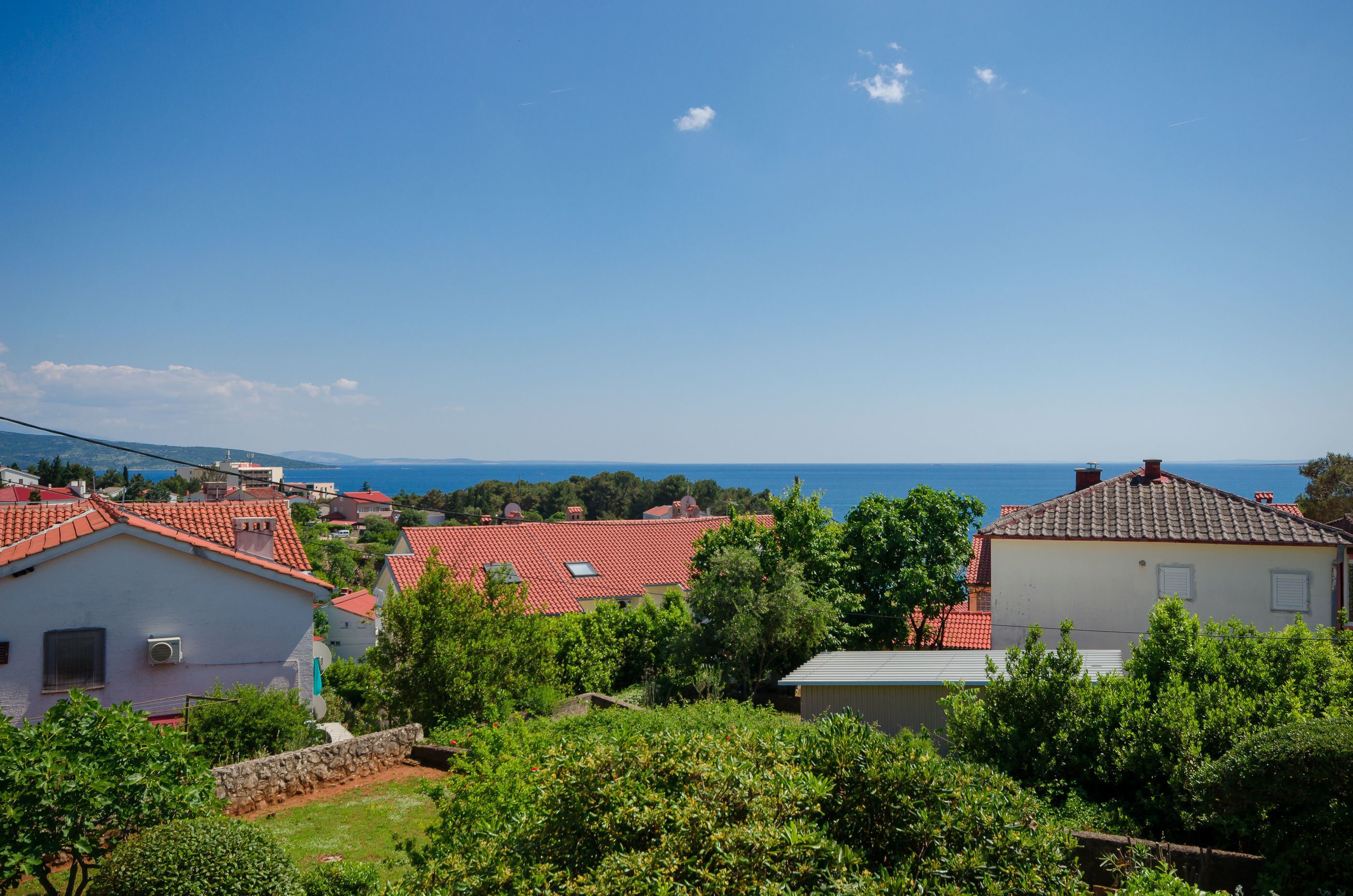 A coastal residential area with houses, greenery, and a clear view of the sea.