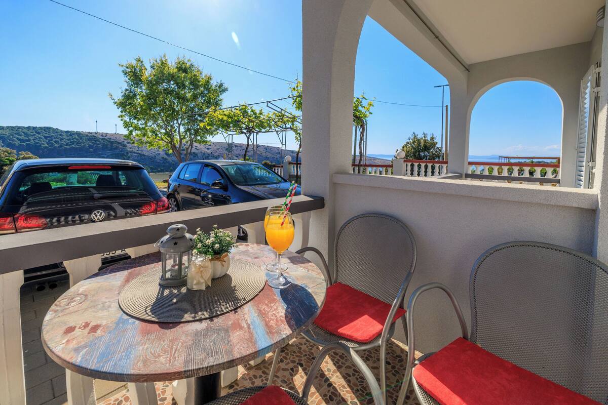 Un balcon avec une table, des chaises et une vue sur les voitures garées et les collines.