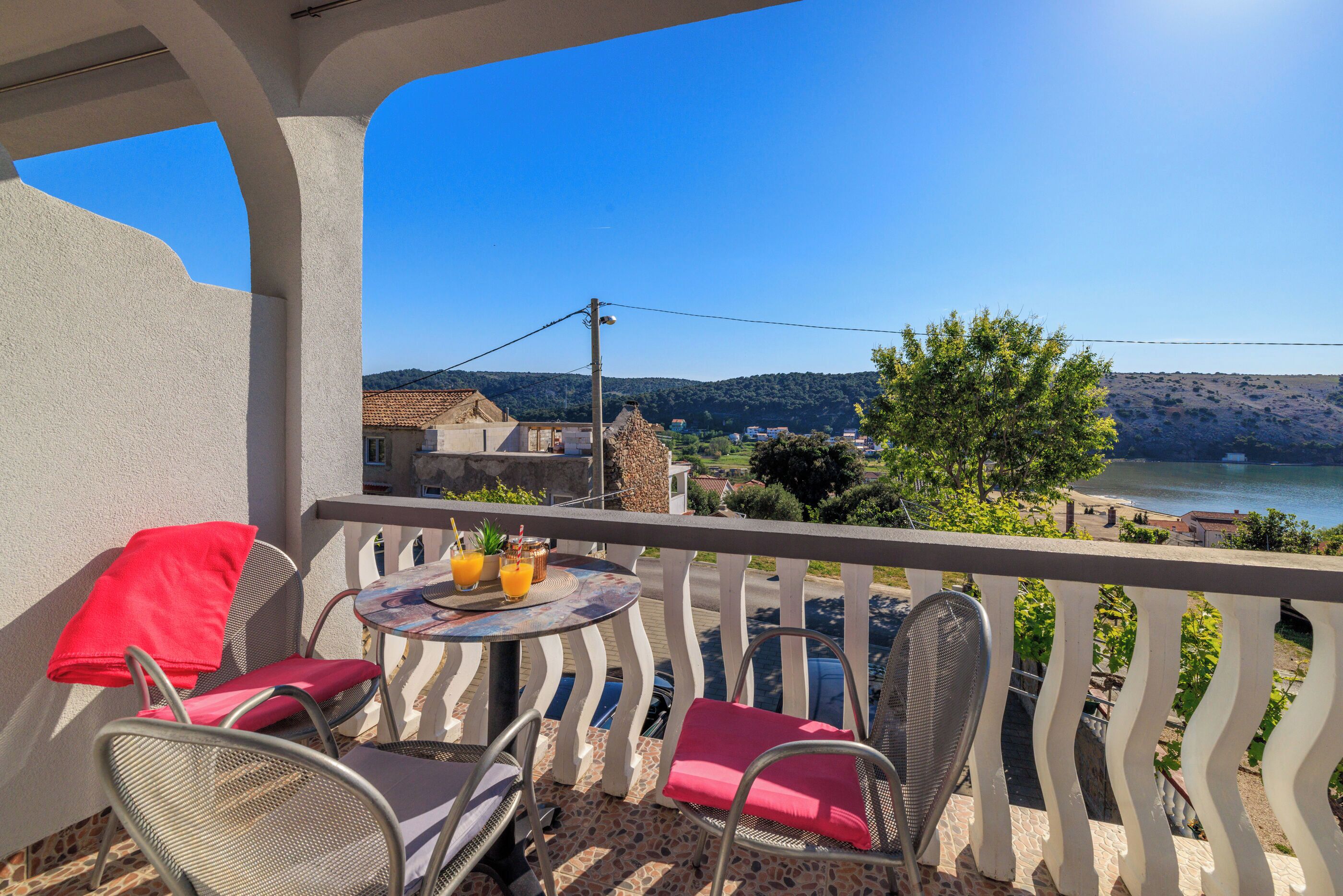 A balcony with a table, chairs, and a view of a lake and hills.
