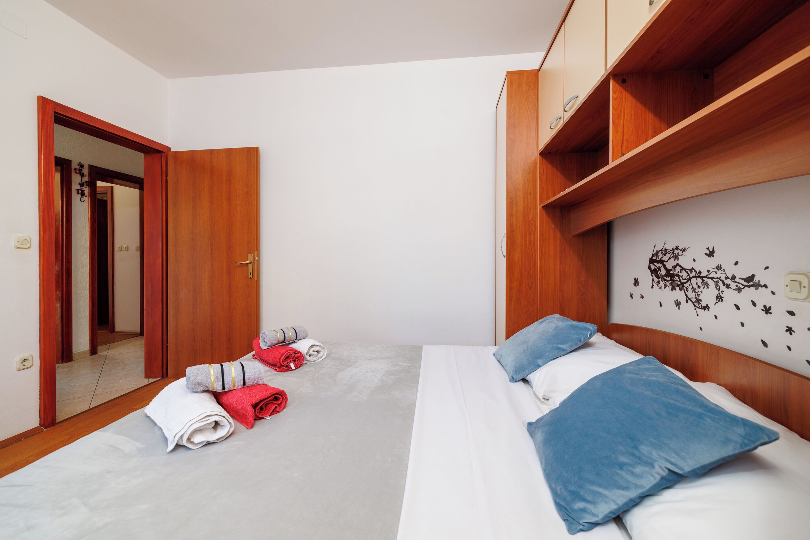 A hotel room with a bed, a wooden wardrobe, and a mirror.