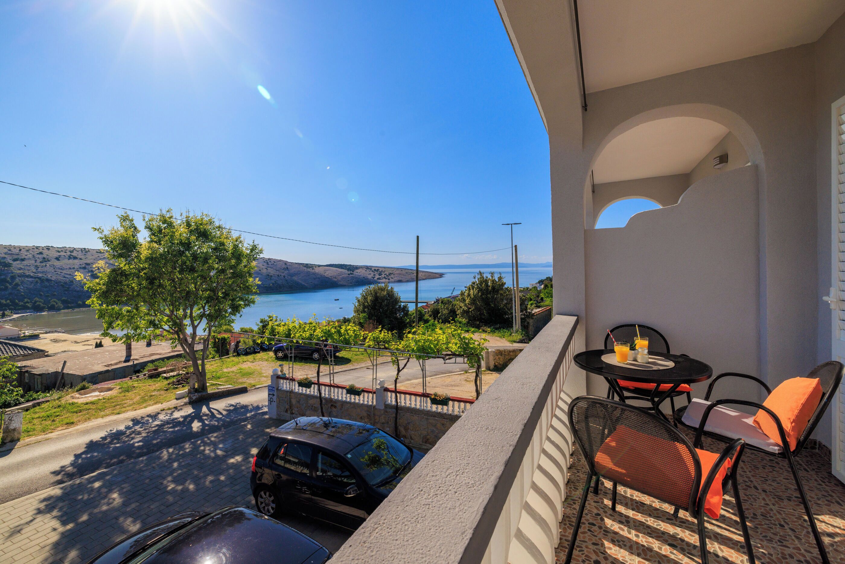 A balcony with a table and chairs, overlooking a road and a body of water.