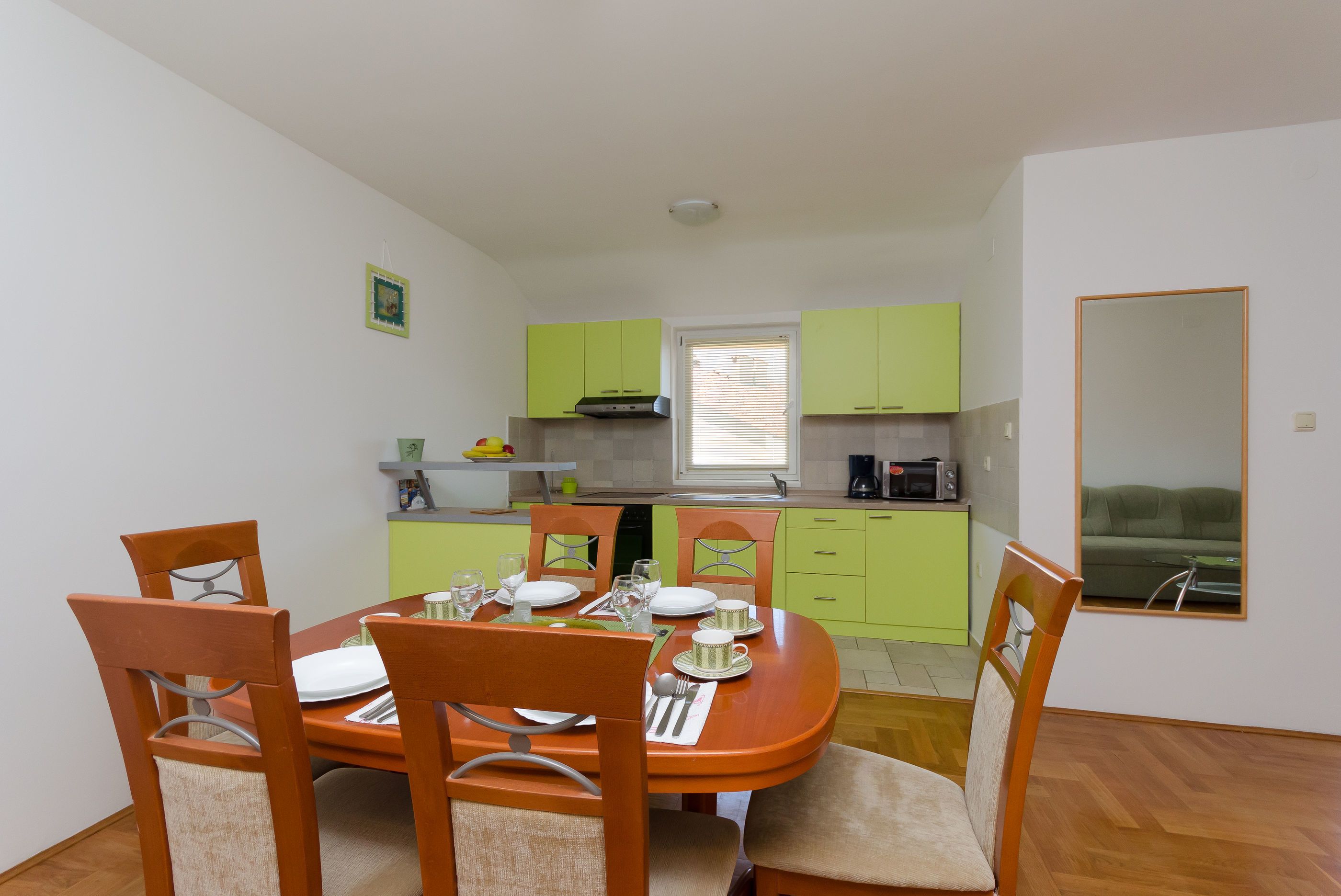 A compact kitchen with green cabinets, a dining table set for four, and a window with blinds.