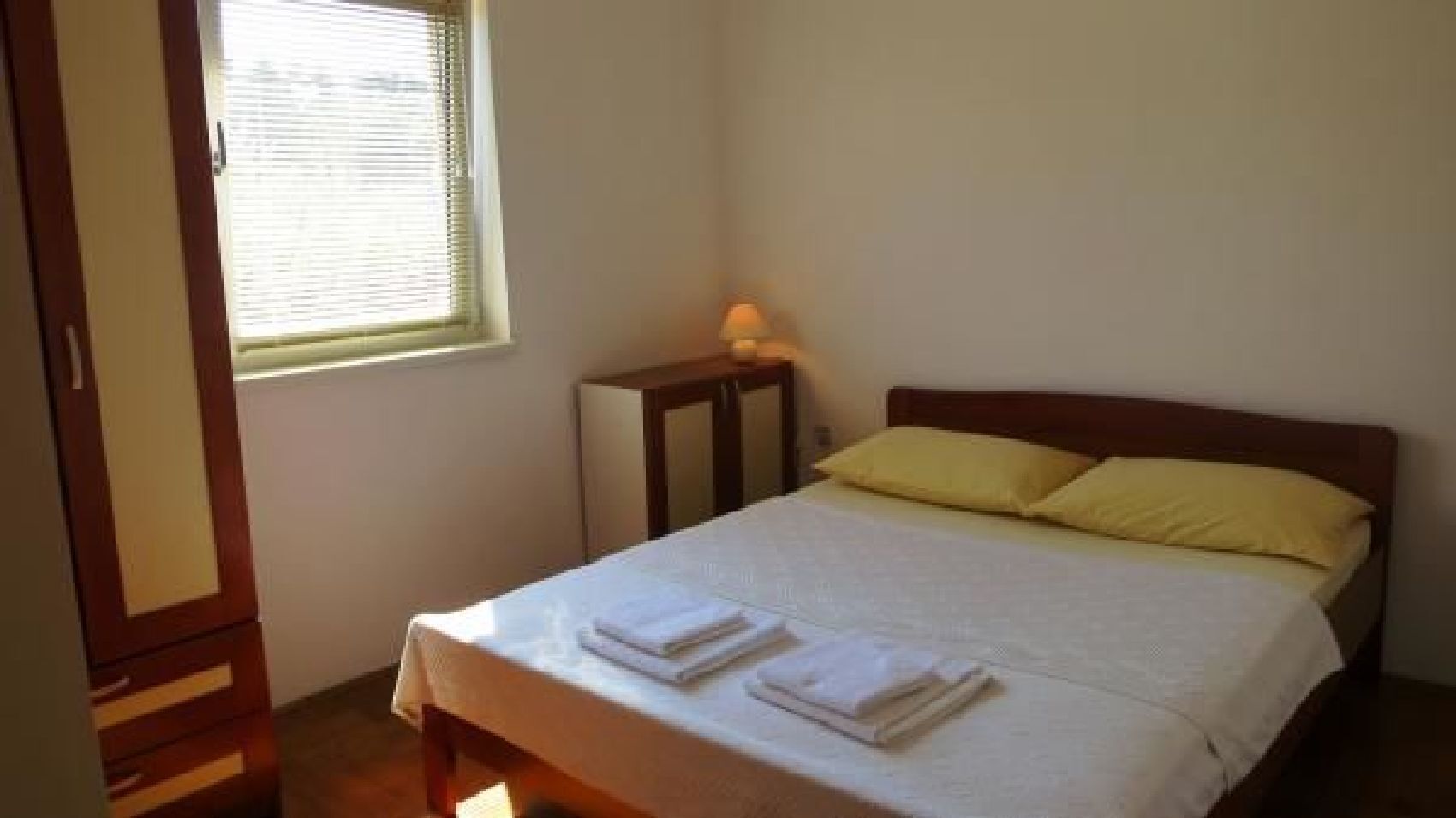 Ein Schlafzimmer mit Bett, Kissen, Nachttisch und einem Fenster mit Jalousien.