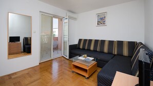 Un salon comprenant un canapé, une table basse, un téléviseur et une porte coulissante donnant sur un balcon.