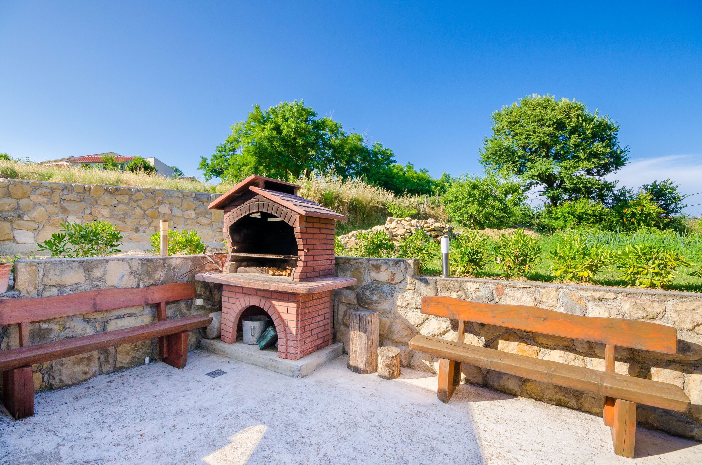 Ein Außenbereich mit Grill, Backofen aus Ziegeln, Steinmauern und Holzbanken.