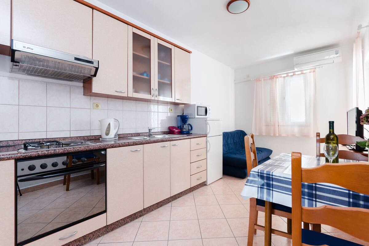 Cucina compatta con piano cottura a gas, forno a microonde e pensili. Sono presenti una zona pranzo con tavolo e sedie.