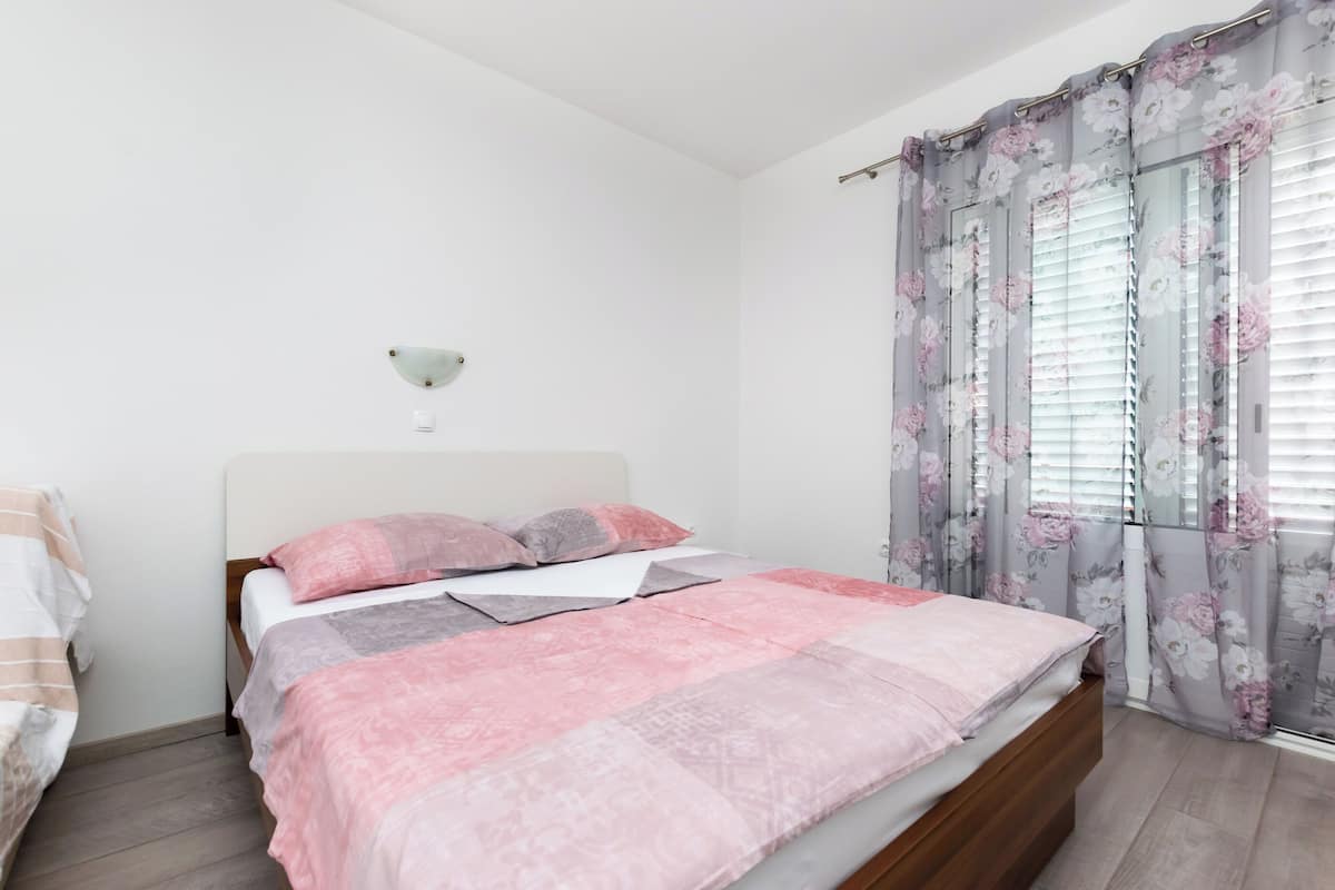 Una camera da letto con un letto, un comodino, una lampada a parete e una finestra con tende floreali.