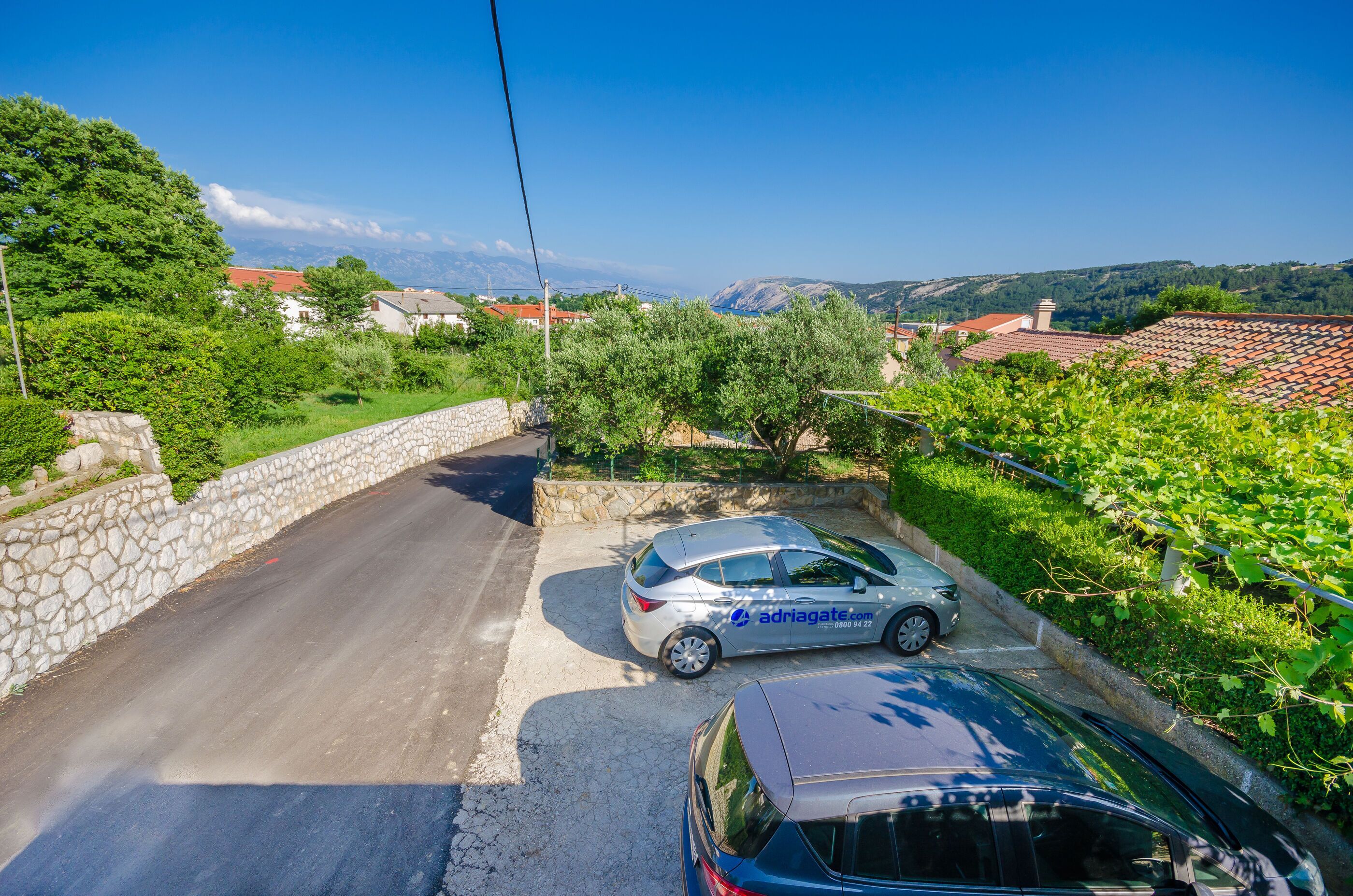 A car parked on a narrow road with stone walls on one side and greenery on the other.