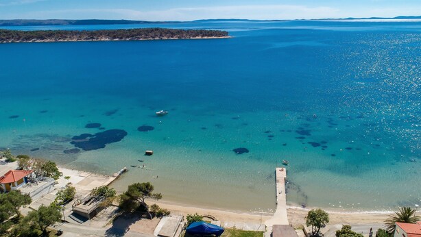 Eine Küstenlandschaft mit klarem, blauem Wasser, einem Sandstrand und einem Steg, der ins Meer ragt.