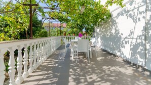 Eine überdachte Terrasse mit weißen Brüstungen, einem Tisch mit Stühlen und einer Pergola mit Weinreben.