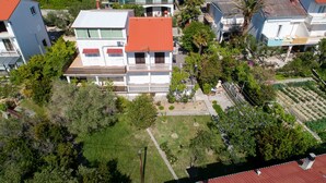 Ein zweigeschossiges Haus mit rotem Dach, umgeben von Grünflächen und weiteren Gebäuden.