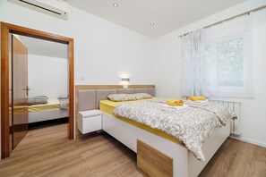 A modern bedroom with a bed, bedside table, and a window with curtains. - Apartments By the sea in Lopar (Lopar)