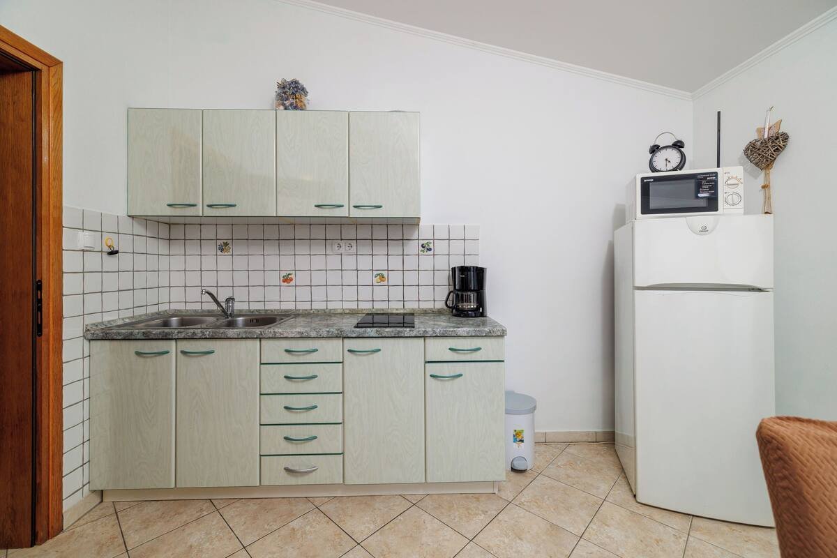 Cocina compacta con armarios de colores claros, un lavamanos, microondas y refrigerador.