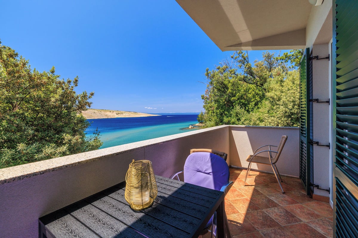 Un balcón con vista al mar, una cesta de mimbre y una silla morada.