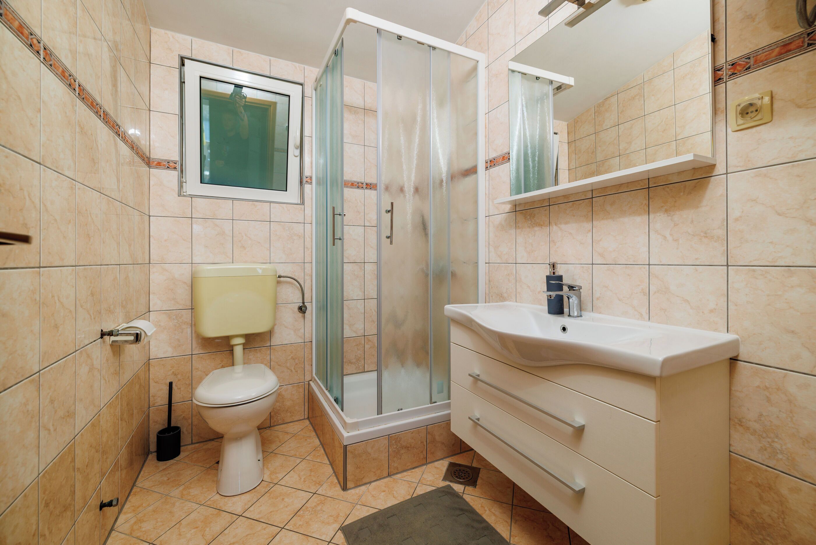 A bathroom with a toilet, shower, sink, and mirror.