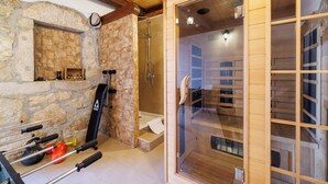 Bany de parets de pedra amb dutxa, sauna de fusta i equip d'exercici.