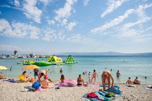 Ein Strand mit badenden und sonnenden Personen, aufblasbaren Spielgeräten und Booten im Wasser.