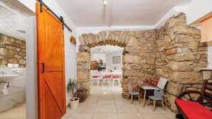 Habitació amb paret de pedra, porta de fusta, zona de dinar amb taula i cadires i una banca.