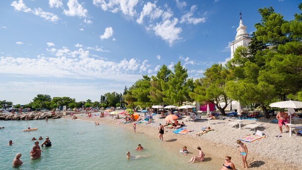 Platja amb gent nedant i prenent el sol, ombrel·les, i un edifici blanc amb cúpula.