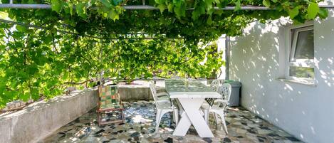 A patio with a mosaic floor, a white table and chairs, and a pergola covered with green vines.