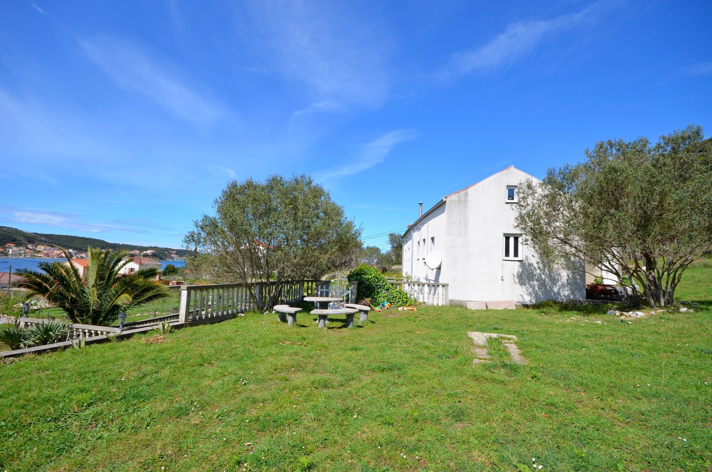 A white building with a sloped roof, surrounded by a well-maintained lawn and a wooden fence.