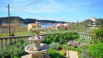 A garden with a stone fountain, a wooden fence, and a view of houses and hills in the background.