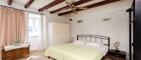 A bedroom with a bed, a nightstand, a dresser, a ceiling fan, and a window with curtains.