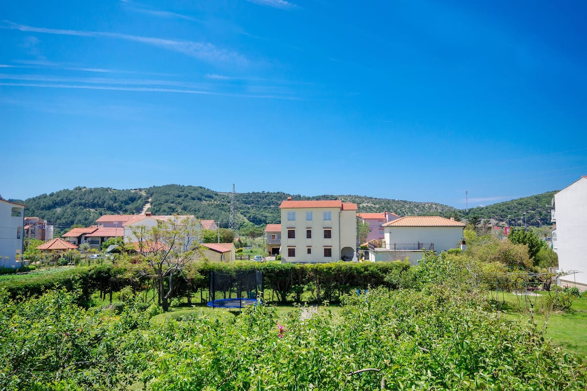 A residential area with houses, a clear blue sky, and a hilly landscape in the background.