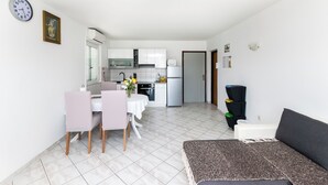 A modern kitchen with white cabinets, a dining area with a table and chairs, and a living area with a sofa. - Apartments Boza (Lopar)