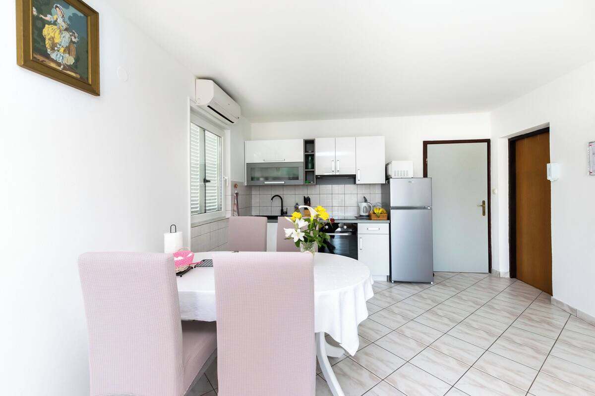 Cocina compacta con armarios blancos, un refrigerador y un comedor con mesa y sillas.