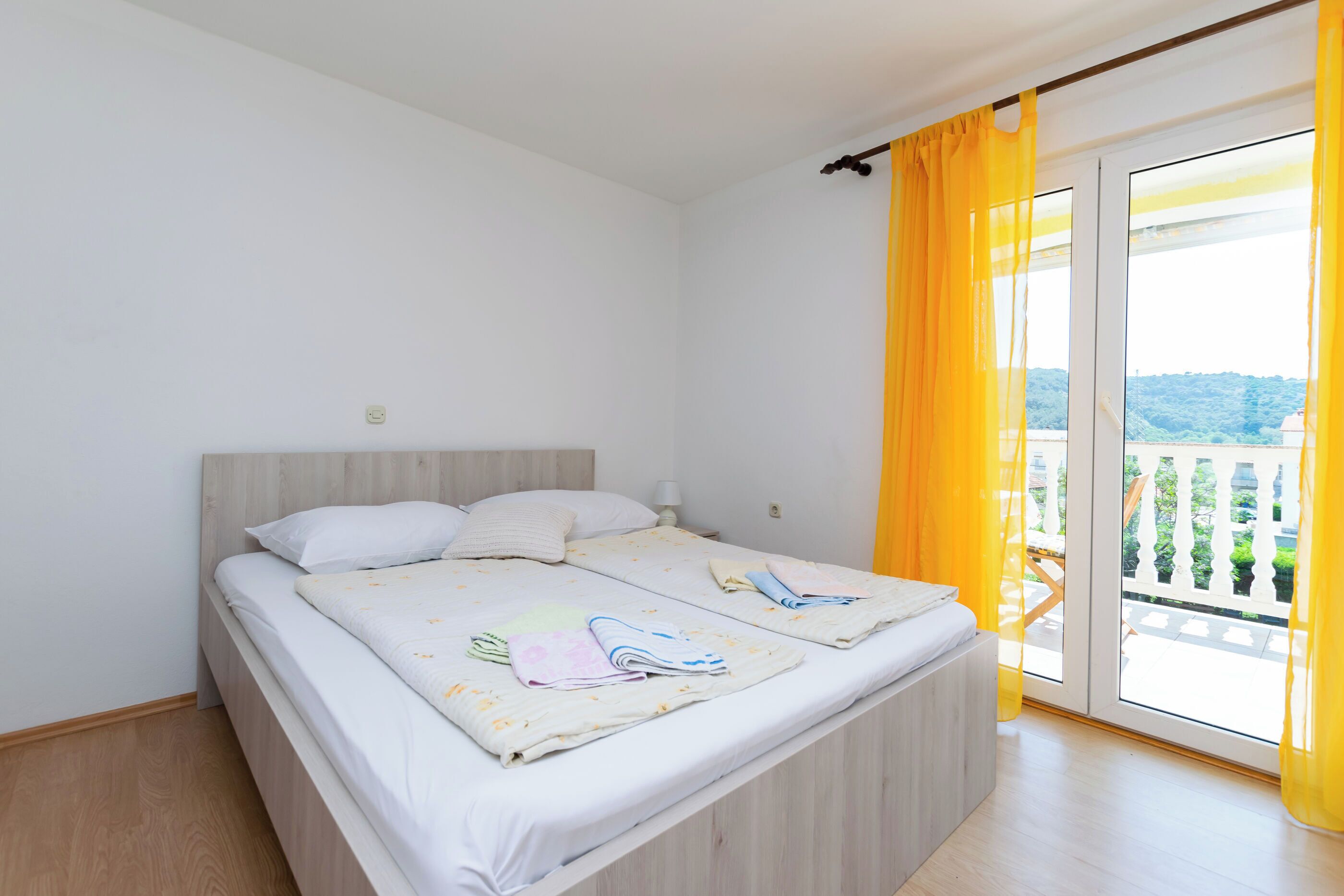 Um quarto com uma cama, janela com cortinas amarelas e vista para o verde lá fora.