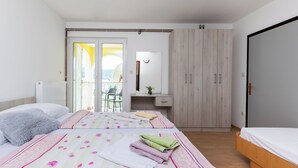 A bedroom with two beds, a wooden wardrobe, a desk, and a view of the outdoors. - Apartments Boza (Lopar)