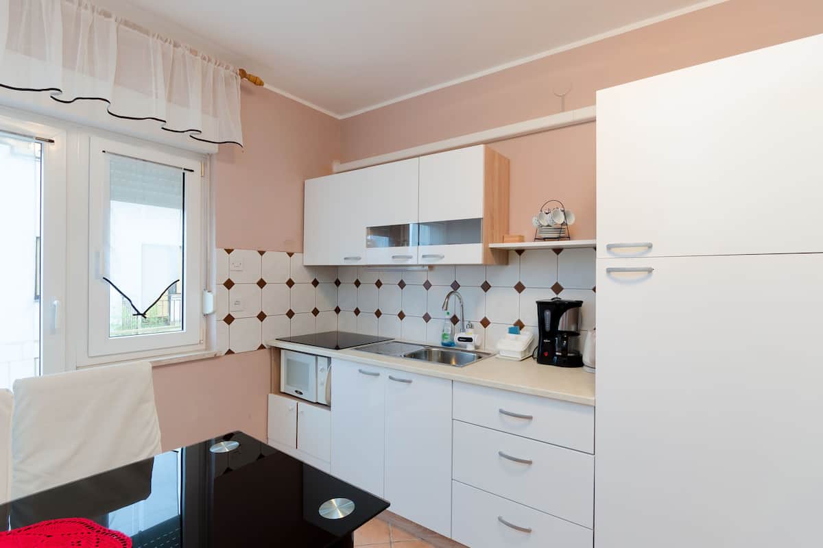 A kitchen with white cabinets, a black countertop, and a window with a white curtain.