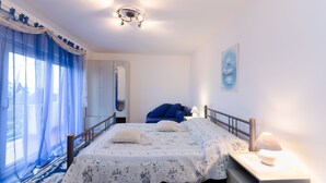 Een slaapkamer met een bed, een nachtkastje, een lamp, een spiegel en een raam met gordijnen.