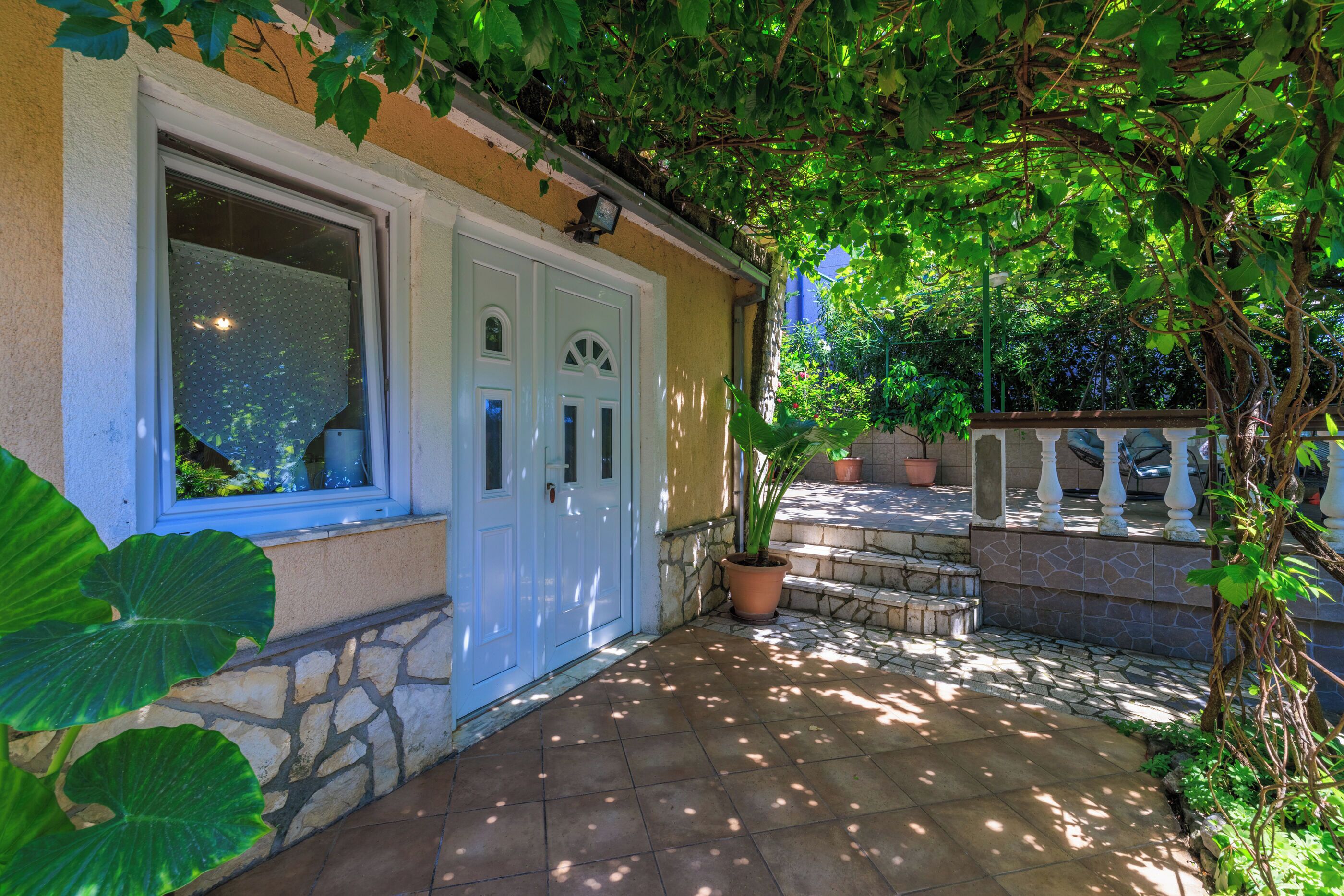 Une maison avec un mur en pierre, une porte blanche et une terrasse carrelée.