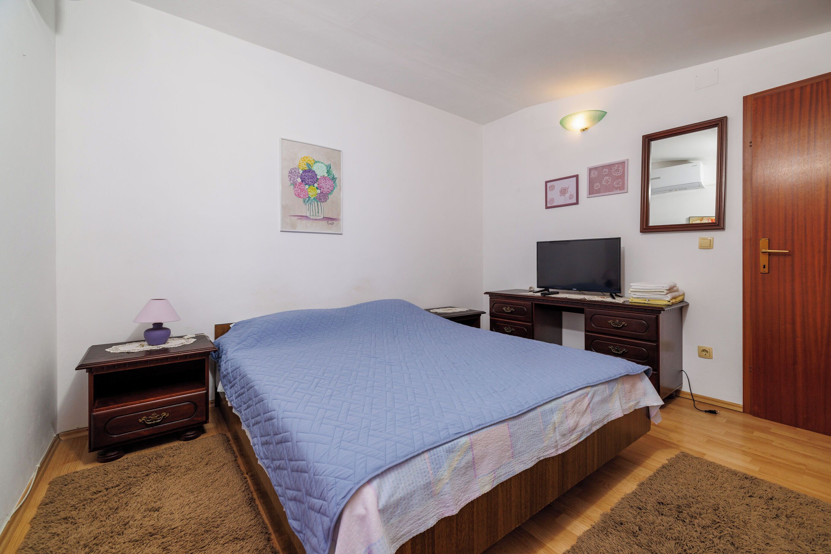 A bedroom with a bed, a desk, a television, and a wooden wardrobe.