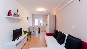 Een moderne woonkamer met een flatscreen televisie, een witte bank en een eethoek met een tafel en stoelen.