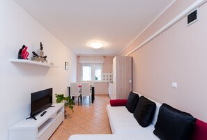 A modern living room with a flat-screen TV, white sofa, and a dining area with a table and chairs. - Apartments and Room Mirjana (Dramalj)