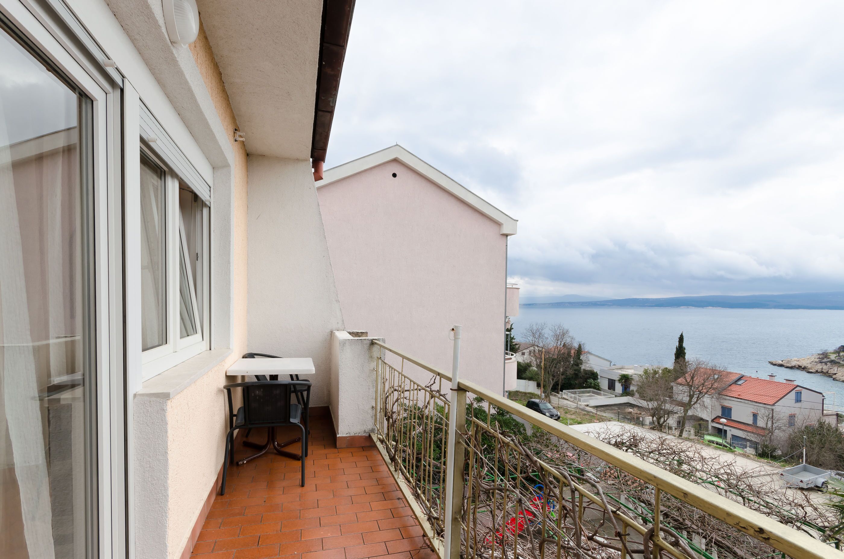 A balcony with a table and chairs, overlooking a body of water and buildings.