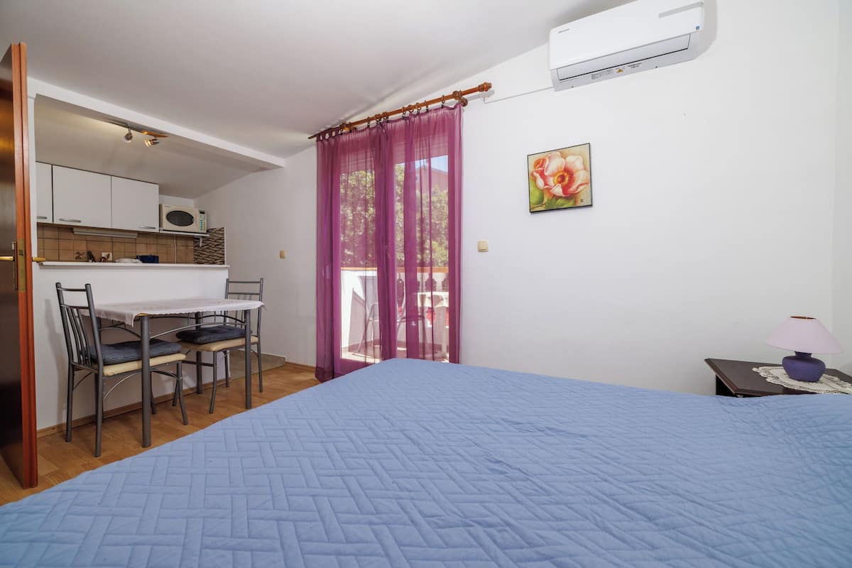 A bedroom with a bed, a desk, and a chair. There is a window with purple curtains and a picture on the wall.