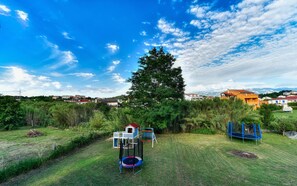 A grassy outdoor area with a swing set, a small playhouse, and a trampoline. - Apartments Helena (Lopar)