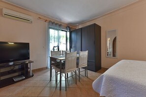 A hotel room with a bed, a TV, a dining table with chairs, a wardrobe, and a window with curtains. - Apartments Helena (Lopar)