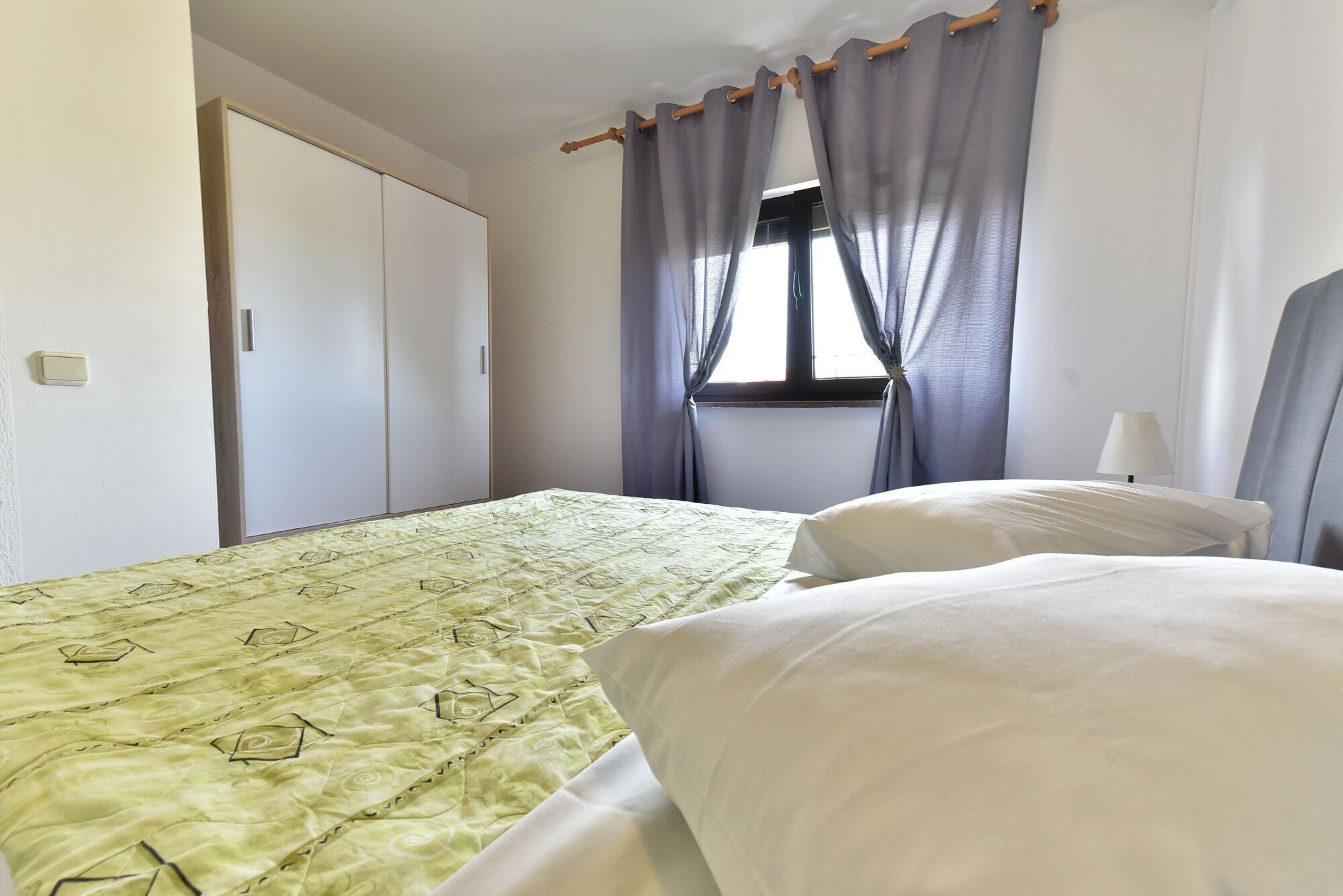 Una camera da letto con un letto, un armadio, una finestra con tende e una lampada da comodino.