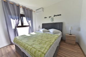 Een slaapkamer met een bed, een nachtkastje met een lamp, een wandairconditioner en een raam met gordijnen.