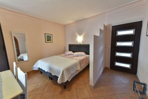 Quarto com cama, cadeira, escrivaninha, espelho, quadro e porta com janelas.