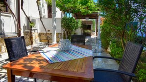 An outdoor patio with a wooden table, two wicker chairs, a striped tablecloth, and a white vase. - Apartments Helena (Lopar)