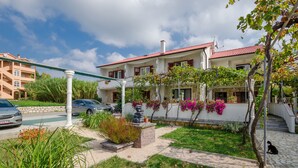 A two-story house with a red roof, white walls, and a garden with flowering plants. - Apartments Helena (Lopar)
